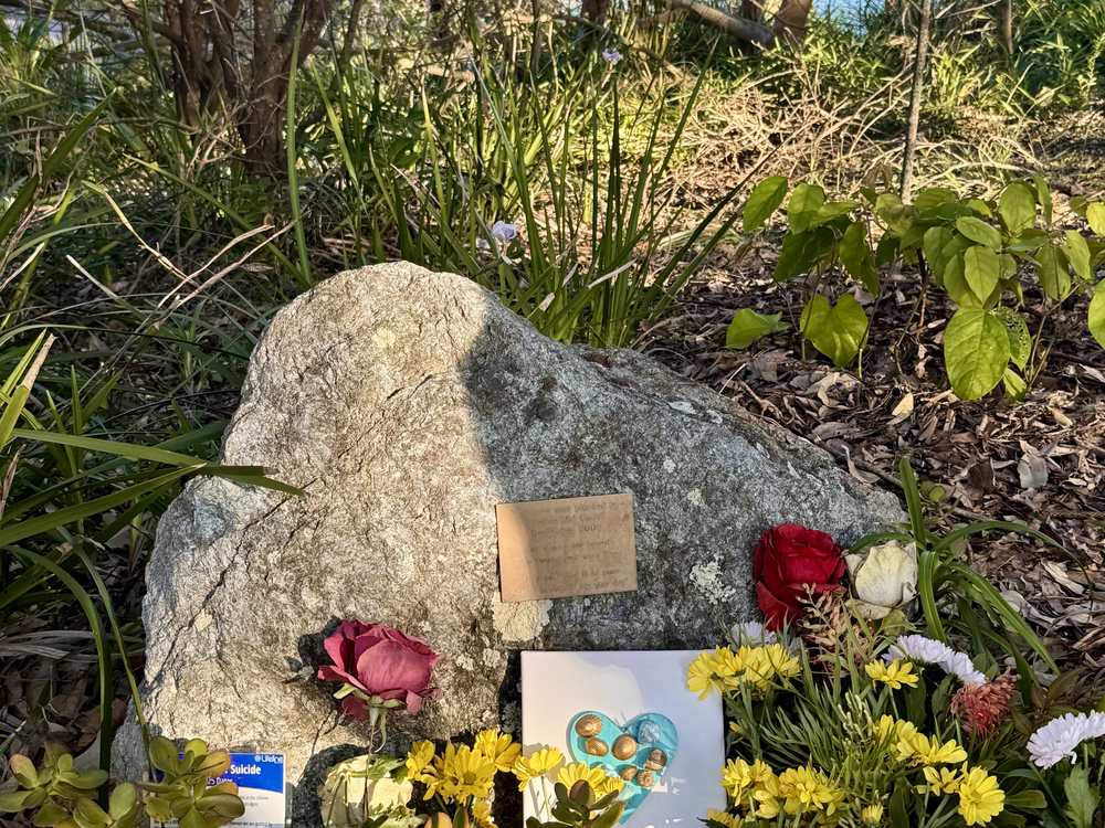 Flowers and a handwritten card left at the foot of a memorial rock