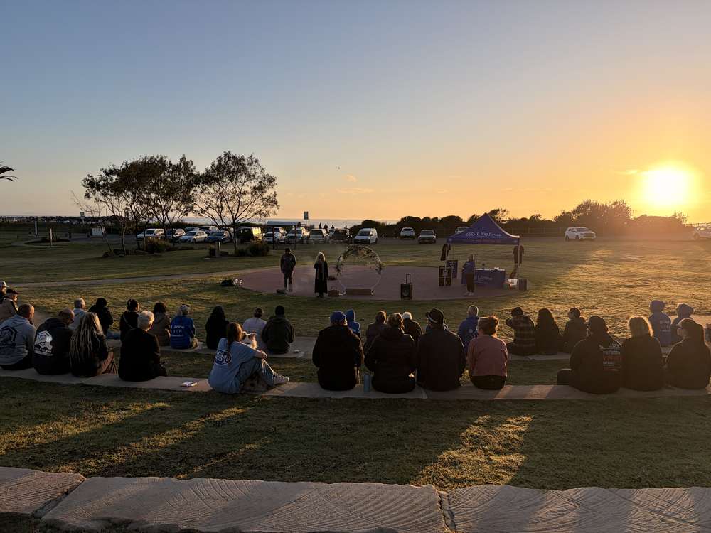 The crowd seated on the grass at the Port Macquarie Amphitheatre as the sun rises behind the stage