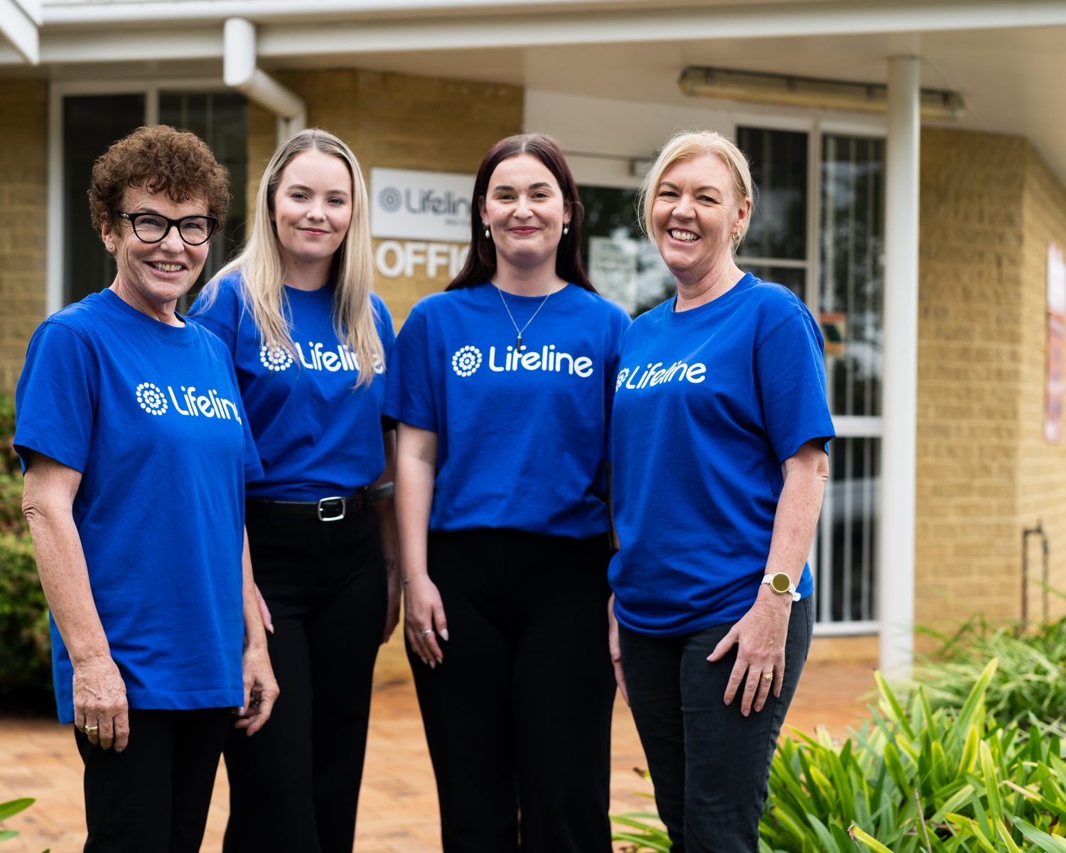 Four smiling Lifeline Mid Coast team members in Lifeline t-shirts outside our Port Macquarie office